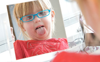 A young girl trying on blue glasses in the mirror